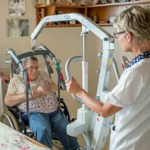 dame en fauteuil levée par un lève personne grâce à une aide à domicile
